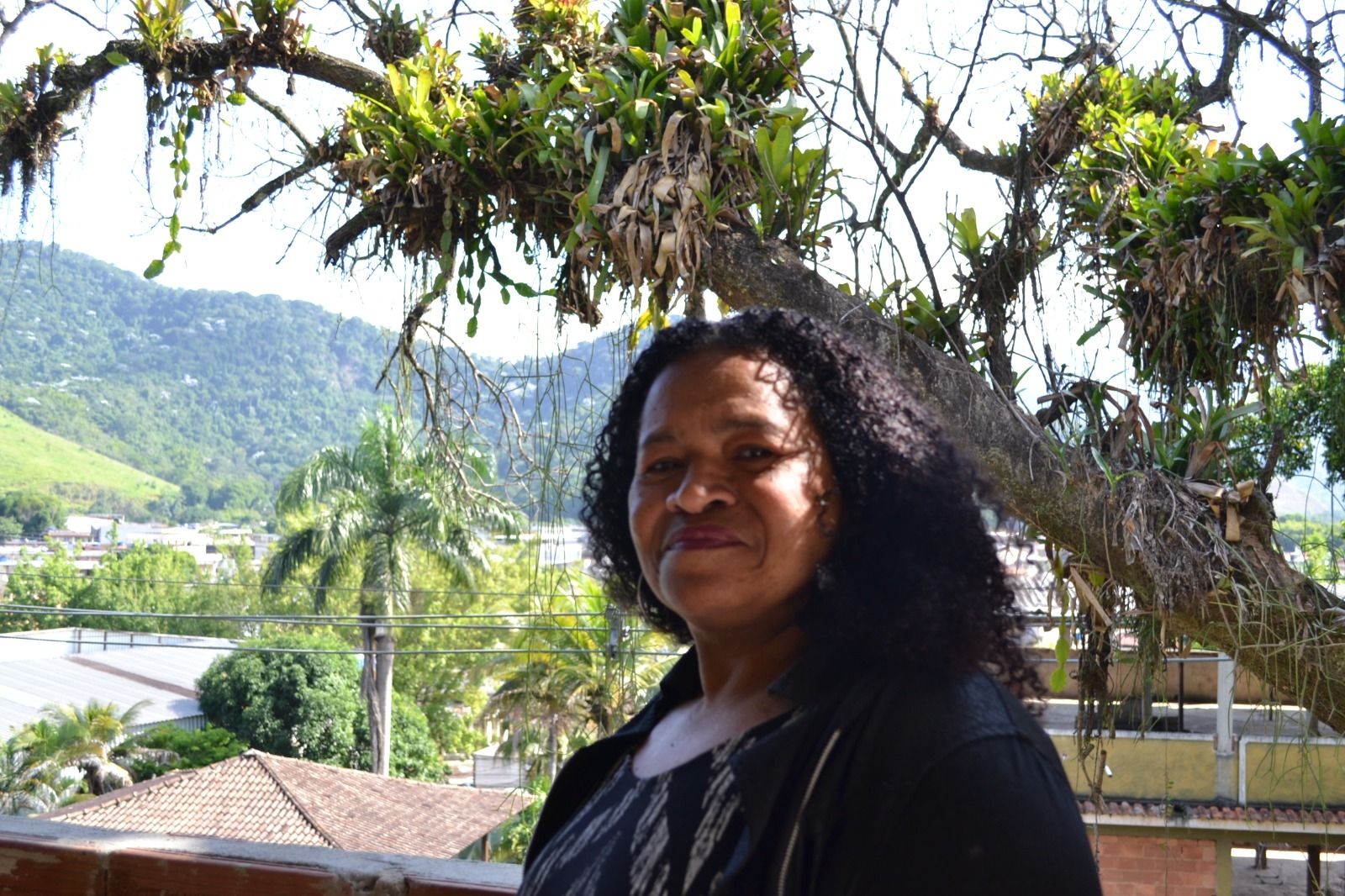 A colunista Rosângela posa no terraço da Rádio Comunitária Serra Verde, em Xerém, com vista privilegiada para a paisagem local.